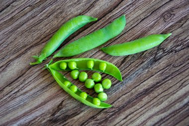 Yeşil bezelye kabukları. Kapsüllerle bitkilere tırmanmak. Bezelyeler ahşap bir arka planda yatıyor. Yukarıdan görüntüle.