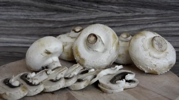 Шампиньоны, цельные и обрезанные, лежат на деревянной доске. Съедобные грибы на столе. — стоковое видео