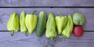 Bulgar biberi. Biber, salatalık ve domateslerin geçmişi. Taze sebzeler ahşap arka planda bir sırada uzanır..