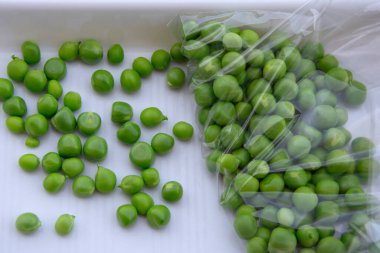 Yeşil bezelyeler beyaz tepside bir torbanın içinde. Yakın plan. Bahçeden taze sebze topluyorum..