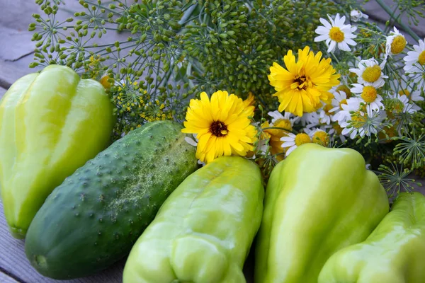 Vegetables and a bouquet of wild flowers. Fresh vegetables on a wooden background. Harvesting in the vegetable garden in summer.