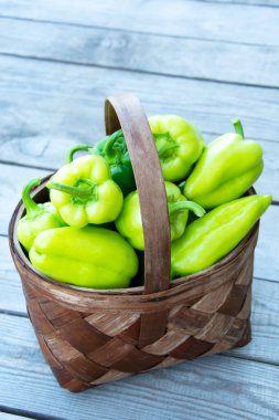 Sepetin içinde sebzeler var. Yeşil dolma biberli bir hasır sepet tahta bir arka planda duruyor. Dikey arkaplan.