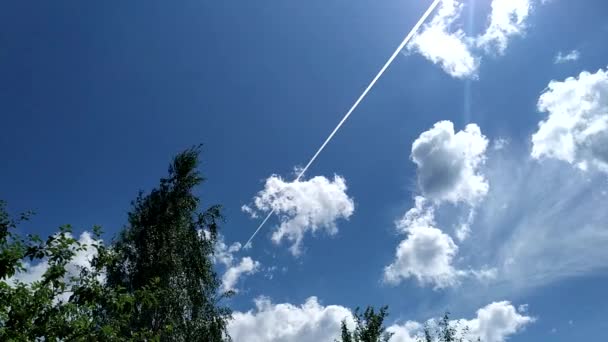 Trilho de avião no céu. O avião voa através do céu azul com nuvens, deixando um rastro branco. — Vídeo de Stock