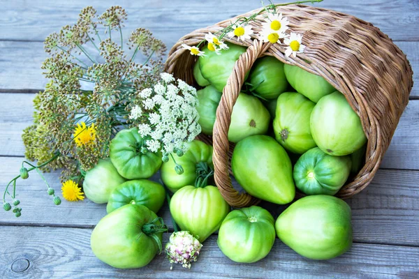 Vegetables in a wicker basket on a wooden background. Basket with fresh vegetables, dill and a bouquet of wildflowers. Harvesting tomatoes and peppers.