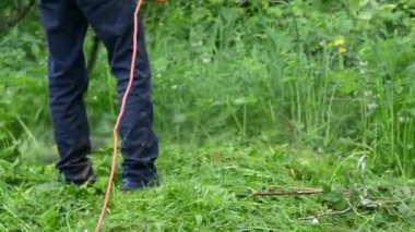 Bir adam bahçedeki kalın çimleri budayarak biçiyor. Uzun çimleri biçmek.
