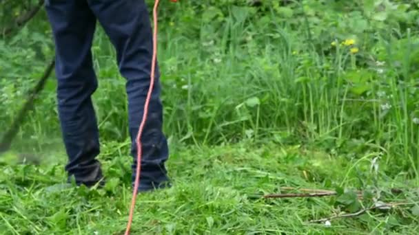 Un uomo falcia l'erba con un trimer elettrico in giardino. Falciatura erba alta. — Video Stock