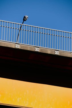 Tamamlayıcı: Açık mavi gökyüzünün altında sarıya boyanmış yol köprüsünün dikey yakın çekimi.