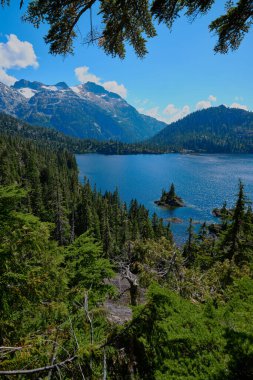 Looking through forest from a rocky outcrop over Bedwell Lake towards a small islet and beyond to the steep, glaciated North flanks of Big Interior Mountain.  Strathcona Park, Vancouver Island, BC, Canada