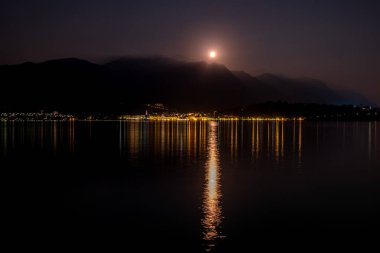 Como Gölü, İtalya 'da gece vakti. Bellagio 'nun parıldayan ışıkları ve dolunay sakin, siyah suya yansıyor.