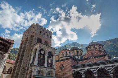 Looking up to the Tower of Hrelyu and cupola-topped main church of Rila Monastery, Bulgaria.  Sun hides behind one white cloud.