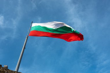 Bulgarian flag flying from flagpole is framed diagonally against blue sky with traces of light, white cirrus cloud