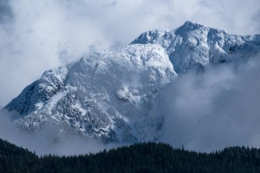 Geçen bulutlar yüzünden karla kaplı tepeler, yoğun ormanlık dağ sırtının ön planında M.Ö. Pitt Gölü 'nün üzerinde uzanıyor.