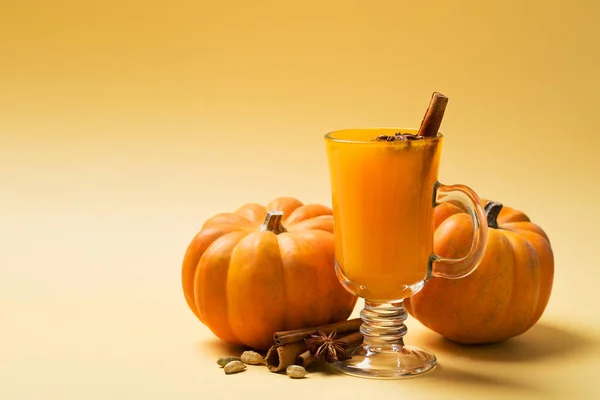 Pumpkins orange coctail drink in glass on yellow background, copy space