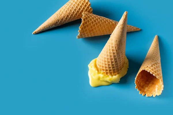Melted yellow ice cream cone creative pastel on blue background, copy space