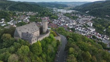 Yeşillik ve arka planda küçük bir kasaba ile çevrili bir ortaçağ şatosunun havadan görünüşü.