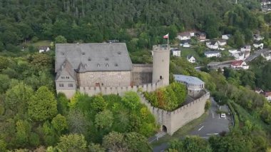 Yeşillik ve arka planda küçük bir kasaba ile çevrili bir ortaçağ şatosunun havadan görünüşü.