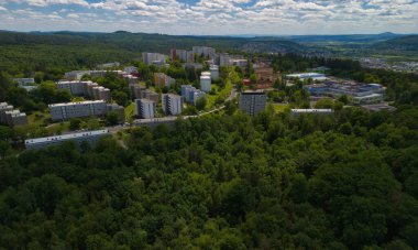 Etrafı yemyeşil orman ve tepelerle çevrili bir yerleşim bölgesinin havadan görüntüsü..