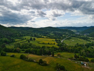 Yuvarlanan tepeler, yeşil tarlalar ve bulutlu gökyüzü manzaralı..