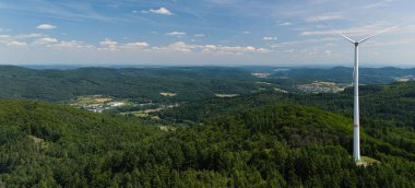 Bereketli yeşil orman manzarasında bir rüzgar türbininin havadan görünüşü.