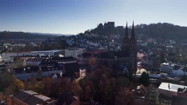 Önde gelen bir kilise ve binalarla dolu bir Avrupa kasabasının havadan görünüşü açık mavi gökyüzünün altında tepelik bir araziye kurulmuş..