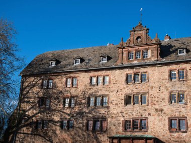 Birden fazla penceresi ve açık mavi gökyüzünün altında açık bir çatısı olan tarihi taş bina..