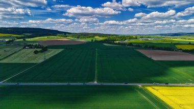 Tarlaları, yolu ve bulutları olan kırsal bir arazinin havadan görünüşü.