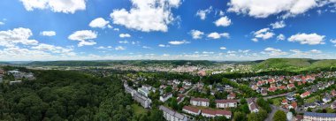 Mavi gökyüzünün altındaki yemyeşil tepelerle çevrili bir kasabanın panoramik manzarası..