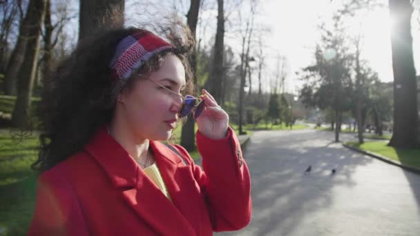 Jolie femme bouclée souriante dans un look élégant lunettes de soleil en toute confiance — Video