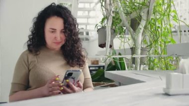 Genç ciddi kıvırcık kız restoranda masada otururken telefonu çeviriyor.