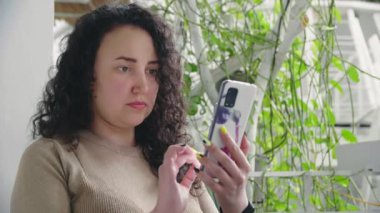 Genç ciddi kıvırcık kız restoranda masada otururken telefonu çeviriyor.