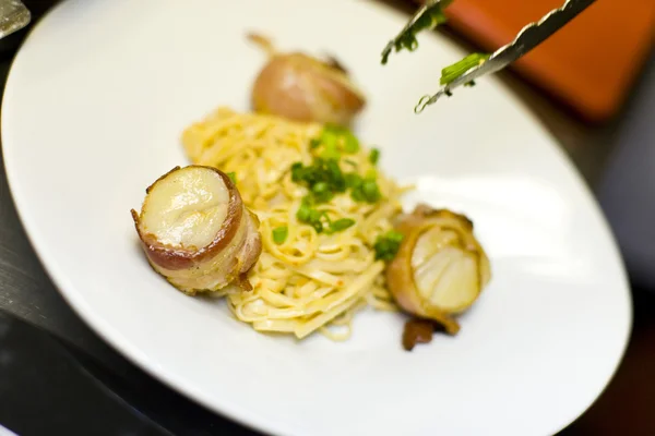 Bacon wrapped scallops and fettuccini with tongs — Stock Photo, Image