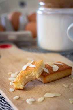 Kısmen yenmiş bir finansör kekinin yakın plan resmi. Kesme tahtasına serpiştirilmiş bademler serpiştirilmiş.