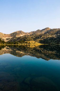 Güneş doğarken Aumar Gölü 'nün panoramik manzarası Neouvielle Doğa Rezervi' nin dağlarını yansıtıyor.
