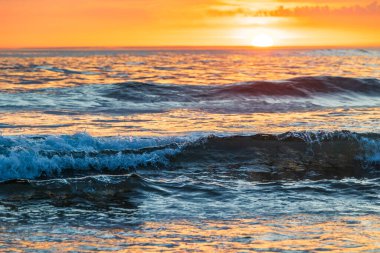 Bretignolles-sur-Mer 'deki La Paree plajının yakınında gün batımının altın ışığıyla vurgulanmış okyanusta dalgalar.