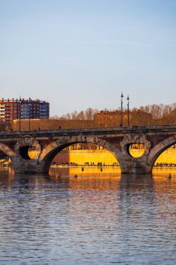 Pont Neuf ve Garonne nehir kıyılarının Toulouse 'da kış günbatımında aylakları aydınlatan manzarası.