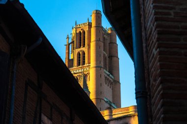 Sainte-Cecile Katedrali 'nin tuğla kulesi Albi şehir merkezindeki dar bir sokaktan gün batımında aydınlandı.
