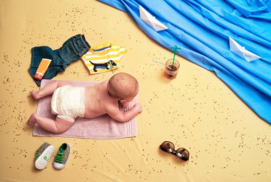 Child lies on a towel on the beach and drinking a cocktail clipart