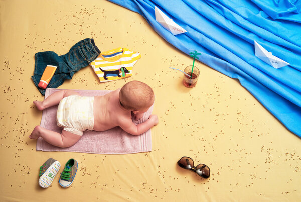 Child lies on a towel on the beach and drinking a cocktail