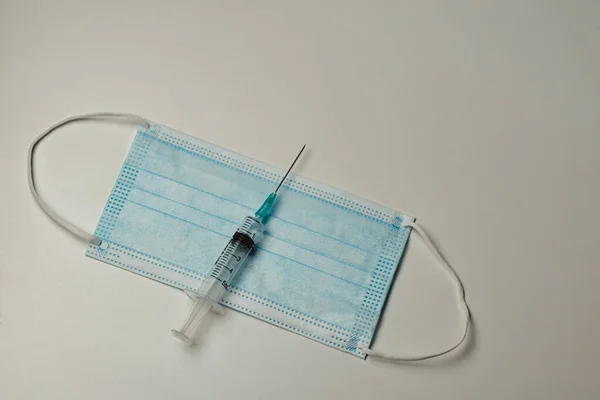 Beyaz arka planda şırınga ve tıbbi maske. Coronavirüs için aşı kavramı