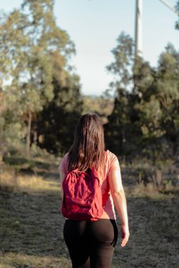 Kırmızı sırt çantalı genç bir Latin 'in doğanın ortasında yürüyüş yaparken çekilmiş dikey bir fotoğrafı. Spor ve eğlence yoluyla sağlık kavramı.