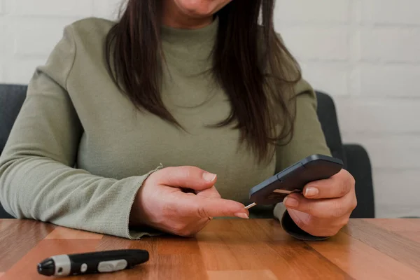 Glukometre kullanan tanınmayan bir Latin kadının ellerinin yakın çekim görüntüsü.