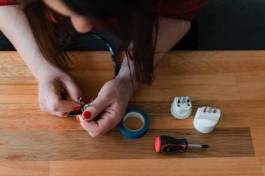 Tornavida kullanan bir kadının el fişini tamir ederken yukarıdan çekilen fotoğrafı.