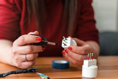 Yetişkin bir Latin kadının ellerinin ön planda çekilmiş bir fotoğrafı. Tırnakları boyalı. Elektrik prizini tamir etmek için tornavida kullanıyor.