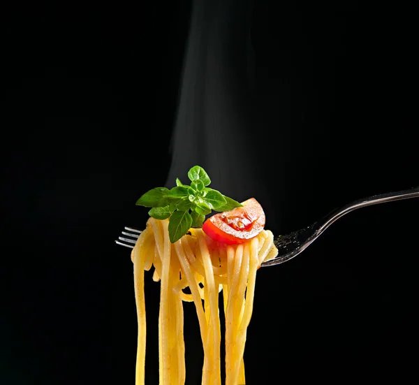 Siyah zemin üzerinde spagetti, domates ve fesleğen bulunan çatal. Buharlı sıcak spagetti.