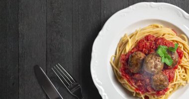Köfteli spagetti, domates sosu ve siyah ahşap arka planda nane yaprağı. Üst görünüm