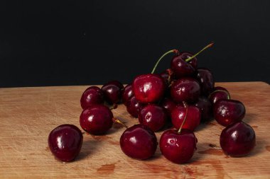 Pile of fresh cherries on wooden desk, black background.