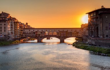 Florence, Italy -20 June, 2019 : view of Ponte Vecchio Bridge glittering in sunset sun rays , river Arno and residential area of the city at golden hour.
