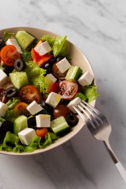 Arka planda beyaz tabakta Yunan salatası. Çatal onun yanında yatıyor. Kahvaltı, atıştırmalık.