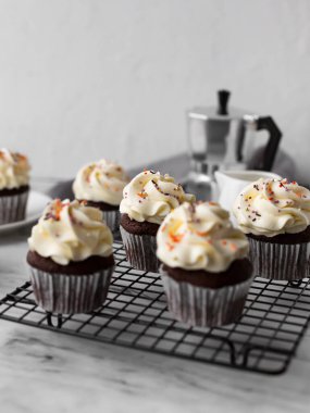 Siyah metal ızgarada çikolatalı kekler arka planda kahve demliğiyle. Kekler şekerlerle süslenir.