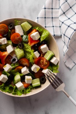 Arka planda beyaz tabakta Yunan salatası. Peçete ve çatal yan yana. Kahvaltı, atıştırmalık.